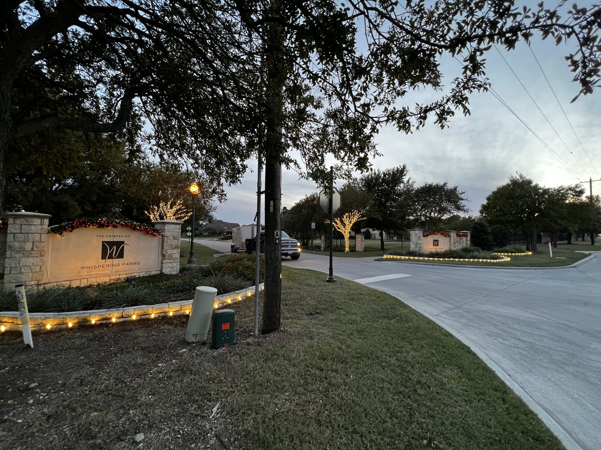 HOA and community Christmas light installation DFW — lit neighborhood monument entrance with garland and wrapped trees