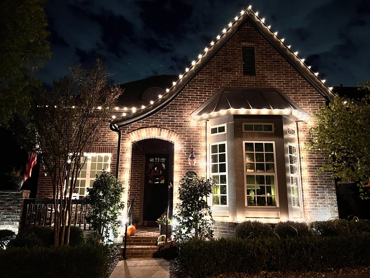 Residential Christmas light installation McKinney TX — warm white roofline and lit wreath on a brick home