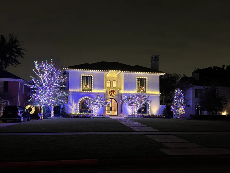 Christmas light installation Dallas TX — warm white roofline and lit wrapped trees on a stucco estate