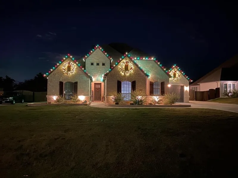 Christmas light installation Denton TX — red and green roofline with lit wreaths on a limestone home