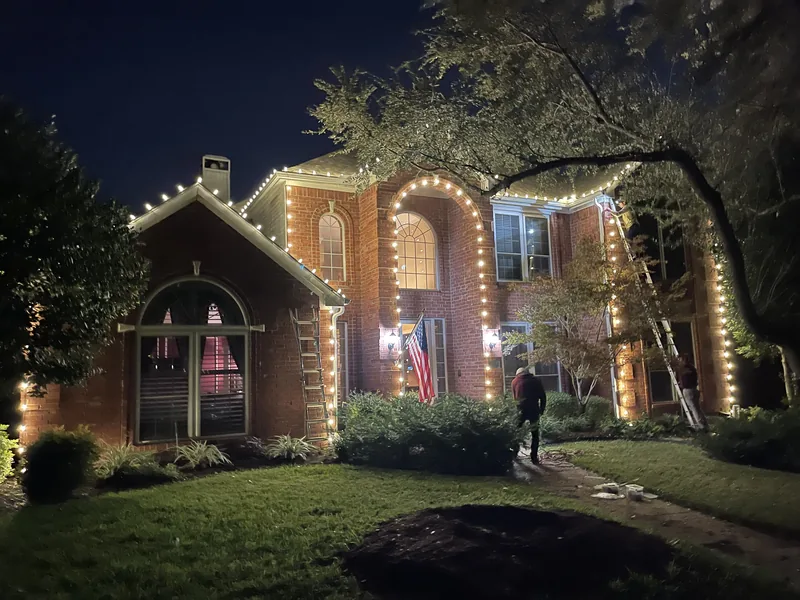 The Christmas Lights Experts crew installing warm white tree wrapping on a Keller, TX luxury home at night
