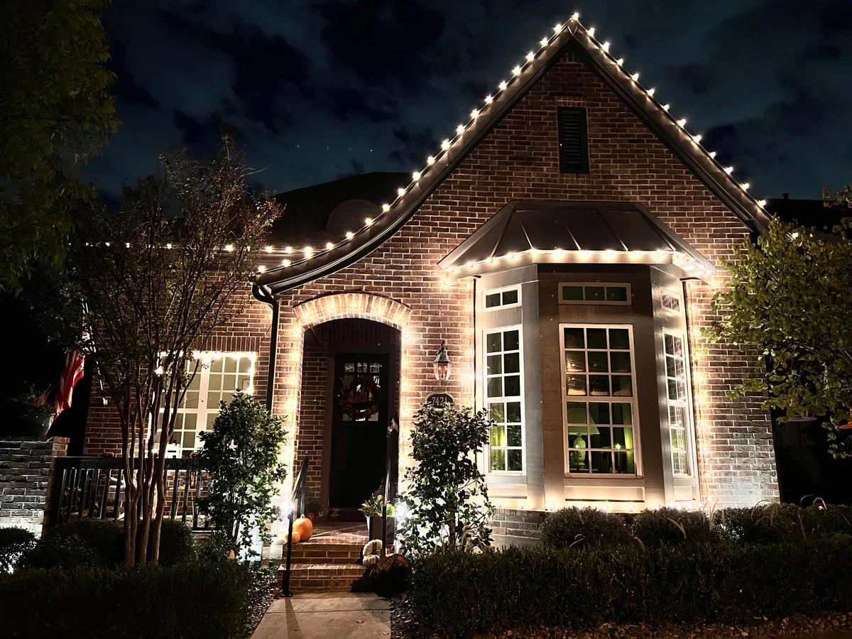 Christmas light installation McKinney TX — warm white roofline and lit bay window on a brick home