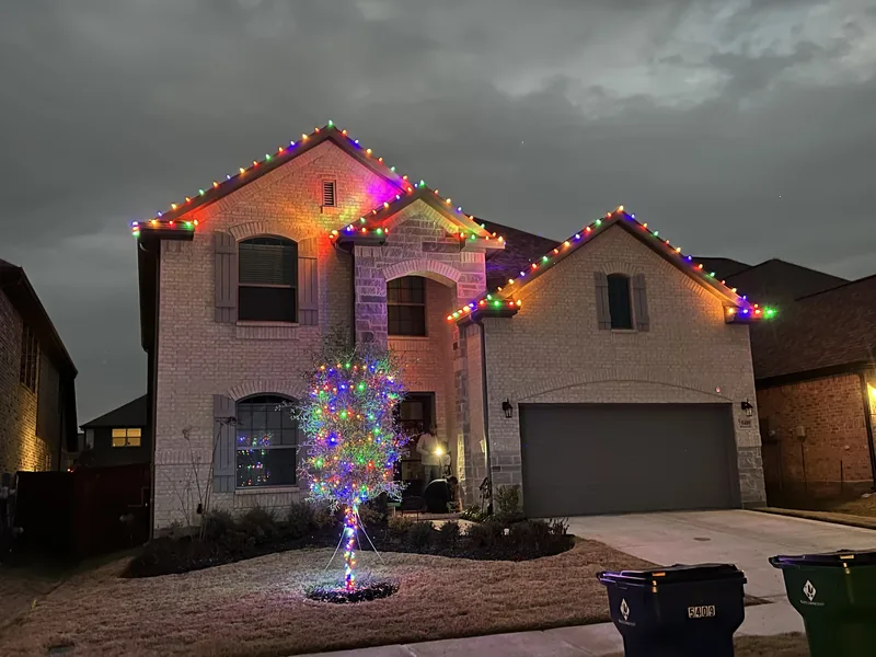 Christmas light installation McKinney TX — multicolor roofline and wrapped tree on a stone home