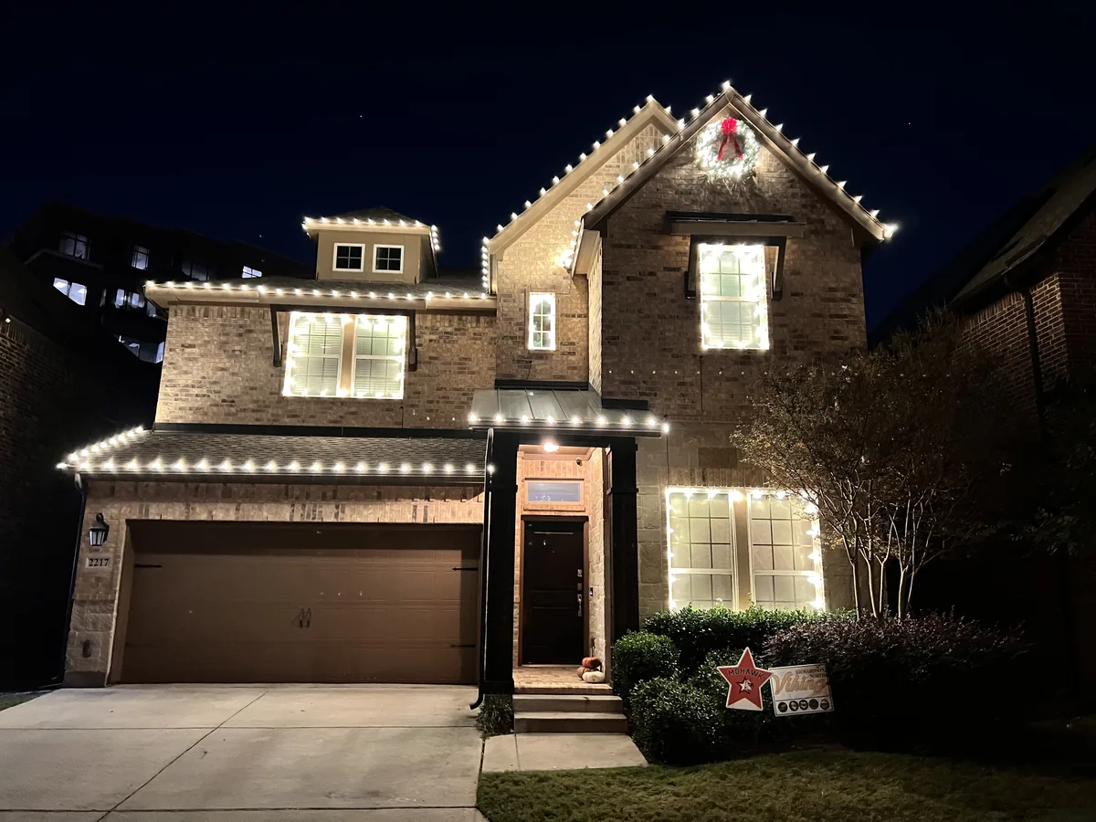 Christmas light installation Richardson TX — warm white roofline and wreath on a two-story brick home